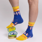 Person wearing blue and yellow anchovy socks resting one foot on a stack of colorful tinned fish cans.