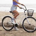Smiling woman seated on a white cruiser bike in the sand, mid-laugh, showing off Coastal Cruiser socks in Mint Heather above patterned high-top sneakers. [lf]