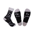 A pair of black crew socks with a grey cuff. The socks feature a white design of open books and the phrases 'Go Away' and 'I'm Reading'.