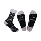 A pair of black crew socks with a grey cuff. The socks feature a white design of open books and the phrases 'Go Away' and 'I'm Reading'.