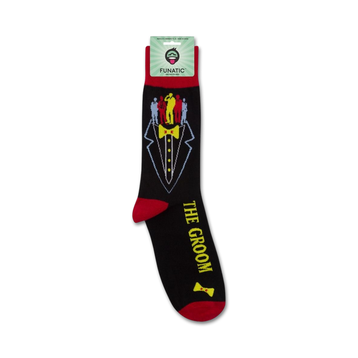 A pair of black socks with a tuxedo printed on them. The tuxedo has a yellow bow tie and a red pocket square. The words 