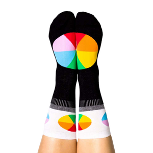 A person's legs with feet up, wearing the black Color Wheel crew socks. The heels show large color wheels, cuffs have smaller ones.
