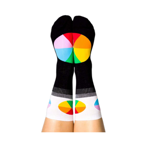 A person's legs with feet up, wearing the black Color Wheel crew socks. The heels show large color wheels, cuffs have smaller ones.