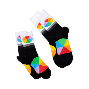 Two pairs of black crew socks with white cuffs and color wheel designs, lying flat and angled differently on a black background.