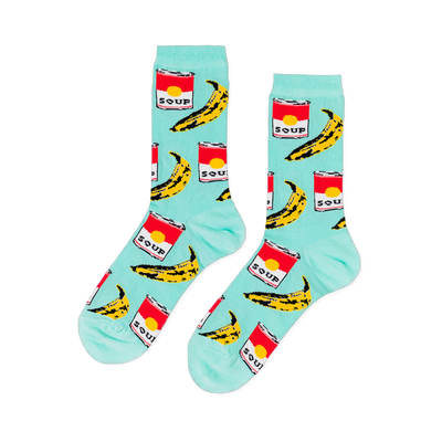 A pair of light blue crew socks with a repeating pop art pattern of red soup cans and yellow bananas, laid flat against a black background.