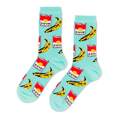 A pair of light blue crew socks with a repeating pop art pattern of red soup cans and yellow bananas, laid flat against a black background.