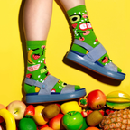 Person's legs wearing fruit-patterned lime green socks and blue sandals, standing on a pile of diverse fruits on yellow. [lf]