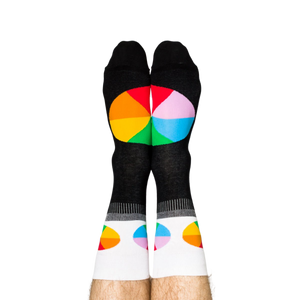 Person standing, wearing black crew socks with white cuffs and colorful, segmented color wheel designs on feet.
