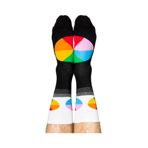Person standing, wearing black crew socks with white cuffs and colorful, segmented color wheel designs on feet.