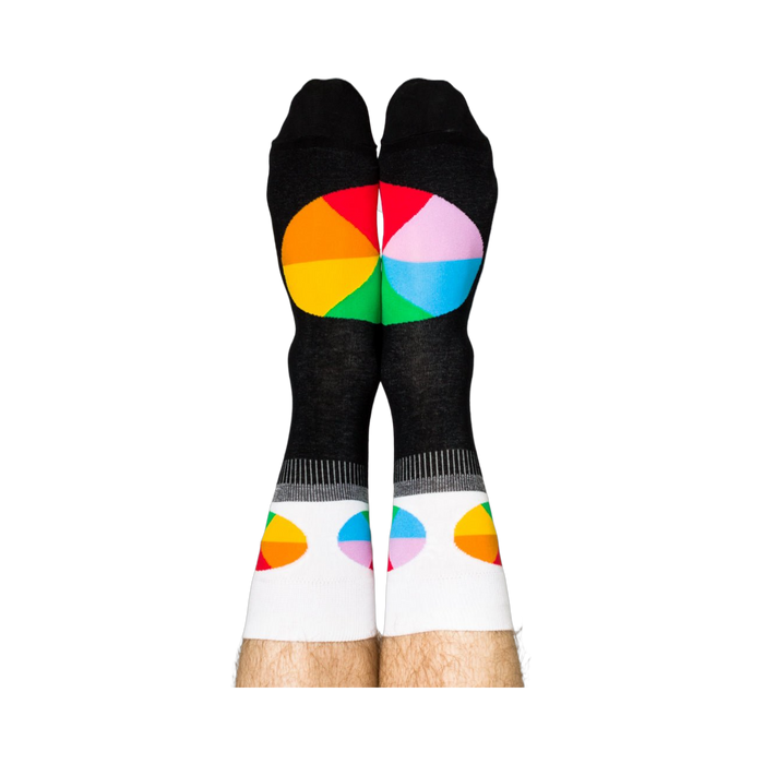 Person standing, wearing black crew socks with white cuffs and colorful, segmented color wheel designs on feet.
