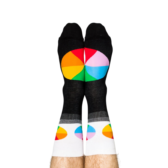 Person standing, wearing black crew socks with white cuffs and colorful, segmented color wheel designs on feet.