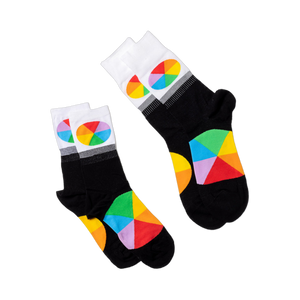Two pairs of black crew socks with white cuffs and colorful color wheel segments, laid flat on a white surface.