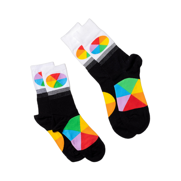 Two pairs of black crew socks with white cuffs and colorful color wheel segments, laid flat on a white surface.