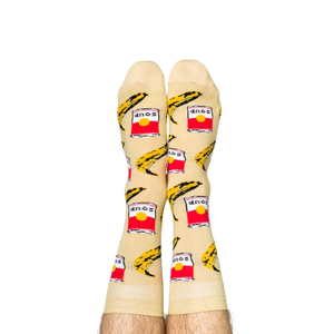 Person wearing Pop Art socks with red soup cans and yellow bananas, shown on legs from the calves down.
