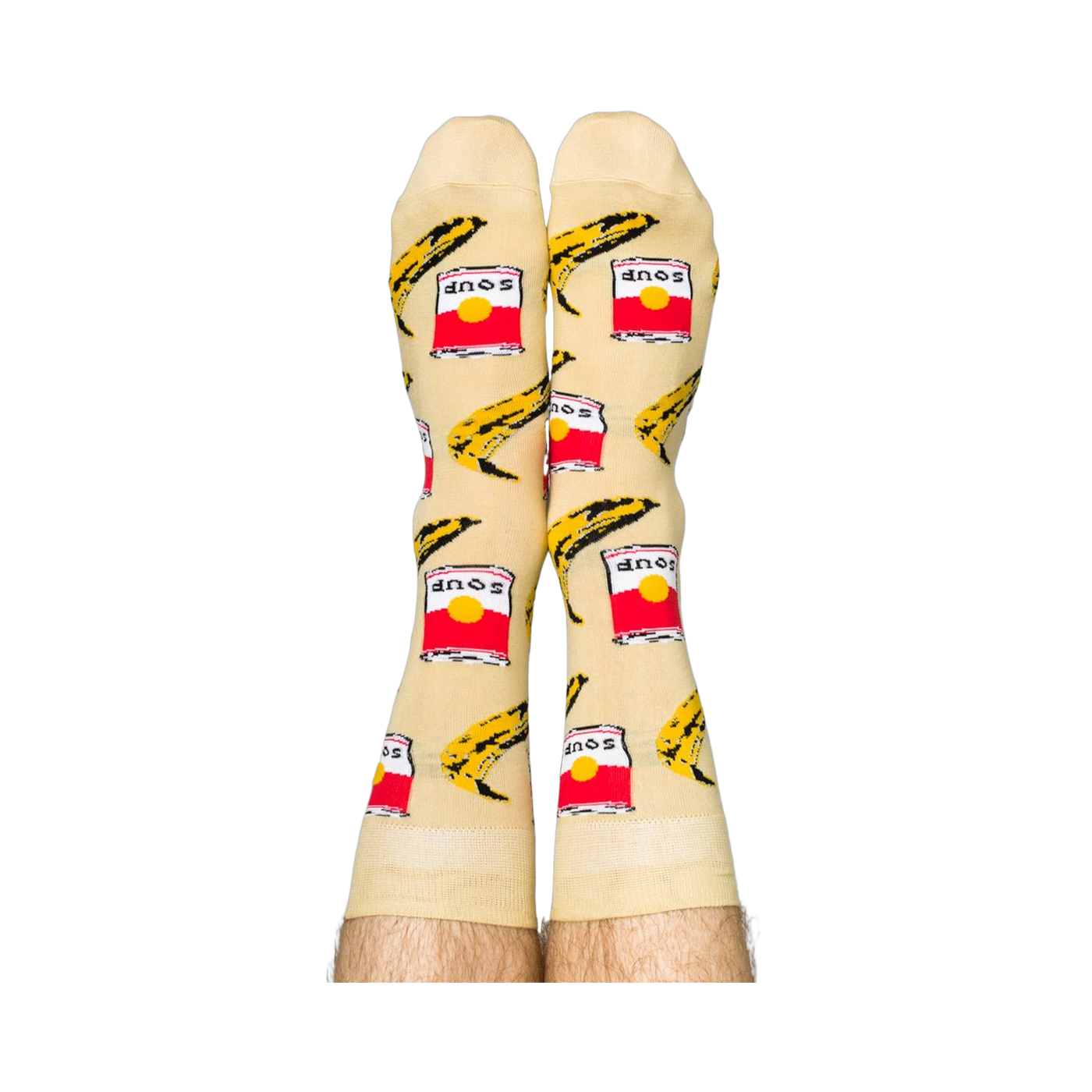 Person wearing Pop Art socks with red soup cans and yellow bananas, shown on legs from the calves down.