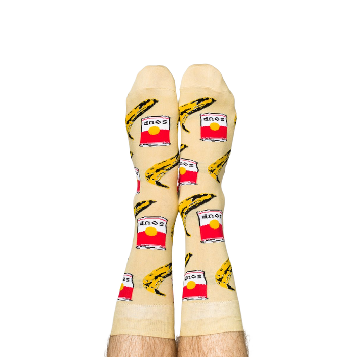 Person wearing Pop Art socks with red soup cans and yellow bananas, shown on legs from the calves down.