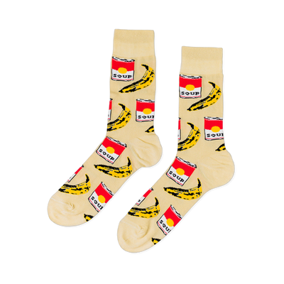 Pair of crew socks with a cream background, featuring a repeating pattern of red soup cans and yellow bananas.