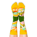 Person wearing the yellow and green socks with their feet up, revealing the words Stay Gold printed on the bottom soles.