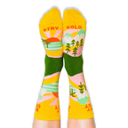 Person wearing the yellow and green socks with their feet up, revealing the words Stay Gold printed on the bottom soles.