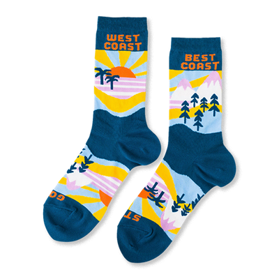 A pair of mismatched crew socks with West Coast beach scenes (sun, palm trees) and Best Coast mountain scenes (peaks, pine trees) on a dark teal base.