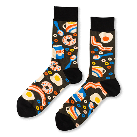 Pair of crew socks with a black background covered in a pattern of fried eggs, bacon, donuts, milk cartons, and coffee cups.