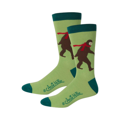 Pair of crew socks featuring a light green background, teal cuffs, and a brown Bigfoot wearing a red scarf.
