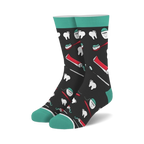 Pair of crew socks with a dark background and teal cuffs.  The design features illustrations of teeth, toothbrushes, toothpaste tubes, and dental floss.