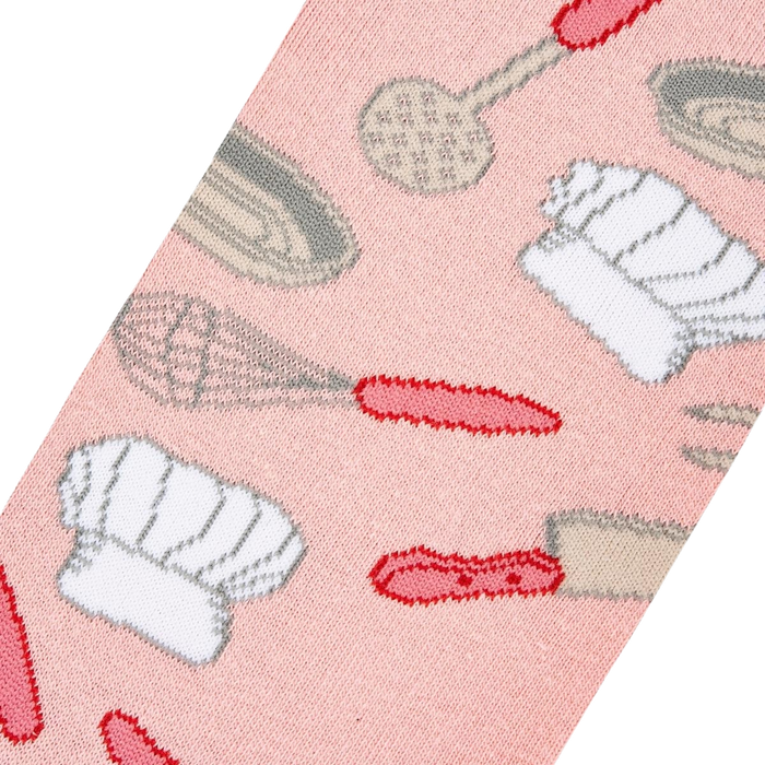 A pink background fabric with repeating pattern of chef hats, spatulas, and whisks in gray and red.