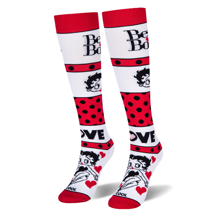 Angled studio shot of Betty Boop knee-high socks standing upright, highlighting the bold red polka dot stripes.