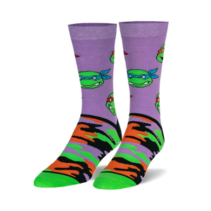 Pair of crew socks. Lavender background with repeating TMNT face pattern and orange, green, and black camouflage print on the lower part. 