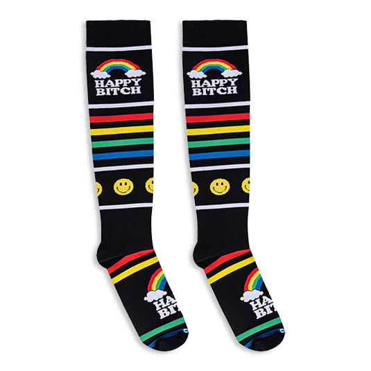 Flat lay of black knee-high socks showing bright rainbow stripes, yellow smiley faces, clouds, and Happy Bitch text.