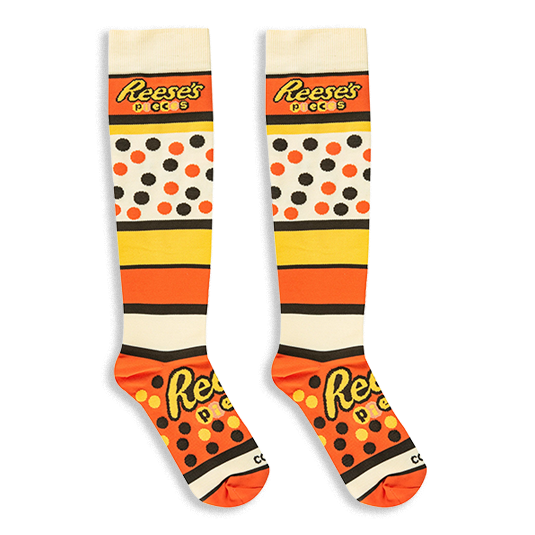 Knee-high Reese's Pieces socks laid flat against a black background, displaying the bold logo text across the foot and calf.