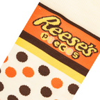 Close-up knit fabric detail showing the Reese's Pieces logo above thick stripes and a field of orange and brown dots.