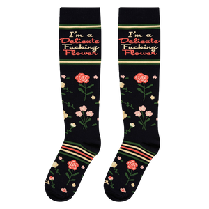 Flat lay view of black knee-high socks showing the full floral pattern and the I'm a Delicate Fucking Flower text.