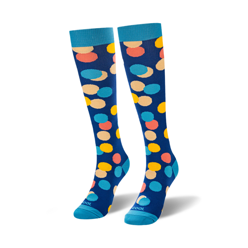 Angled studio shot of two navy blue socks with yellow, coral, peach, and blue dots standing upright with drop shadows.