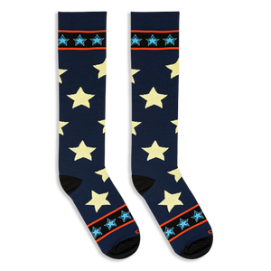 Flat lay of tall navy blue socks with pale yellow stars angled outward to display black toes and striped cuffs.