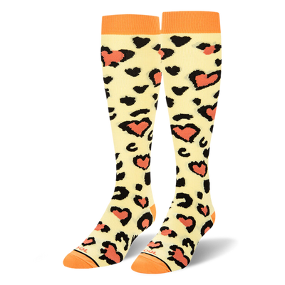 Knee-high socks in pale cream with black leopard print spots surrounding coral hearts, plus solid orange cuffs, heels and toes.