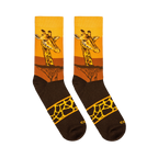 Flat lay of two crew socks displaying a giraffe face over a yellow sunset, dark acacia trees, and a spotted band on the foot.