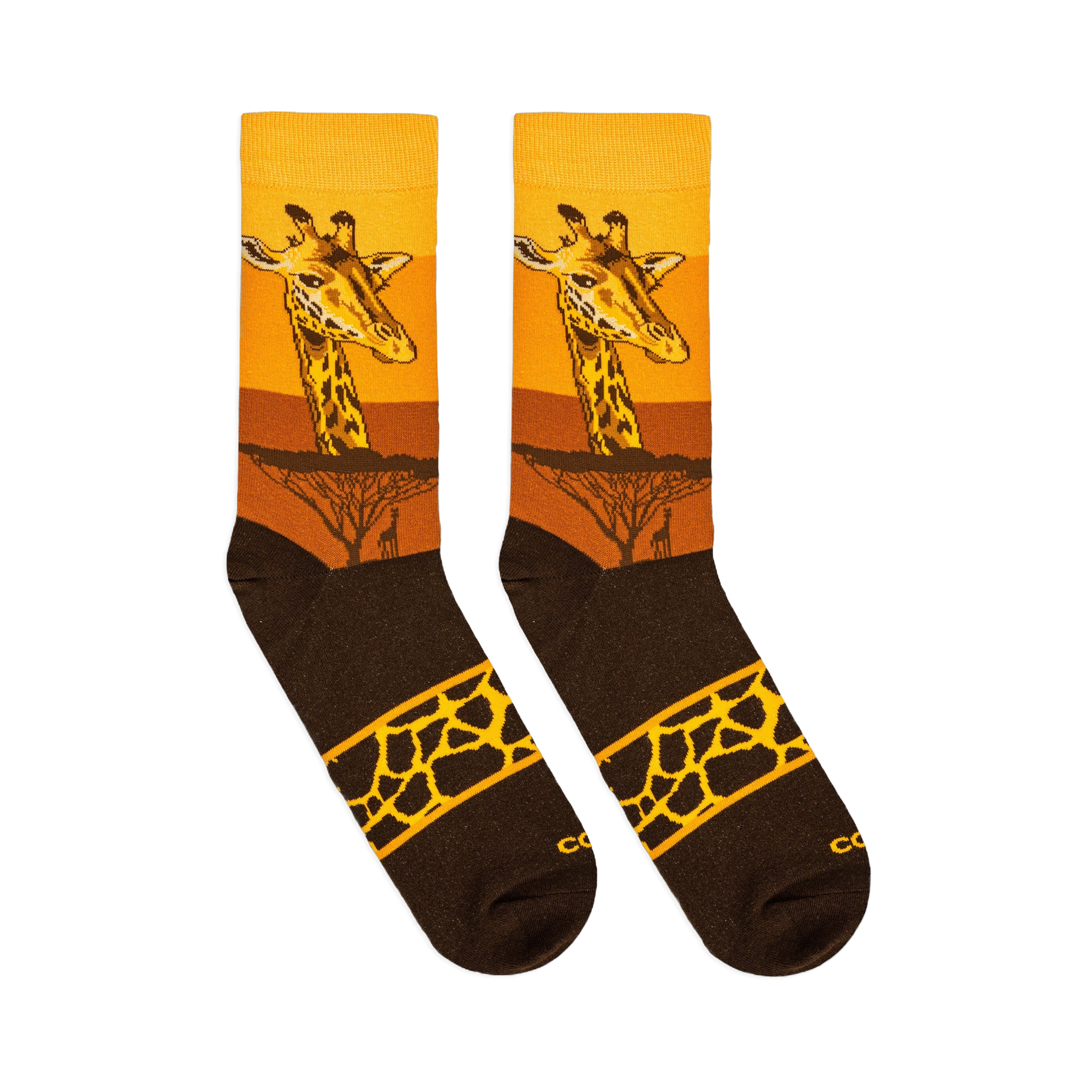 Flat lay of two crew socks displaying a giraffe face over a yellow sunset, dark acacia trees, and a spotted band on the foot.
