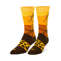 Crew socks showing a giraffe head against a yellow and orange sunset, tree silhouettes, and a brown foot with a spotted band.