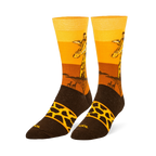Crew socks showing a giraffe head against a yellow and orange sunset, tree silhouettes, and a brown foot with a spotted band.