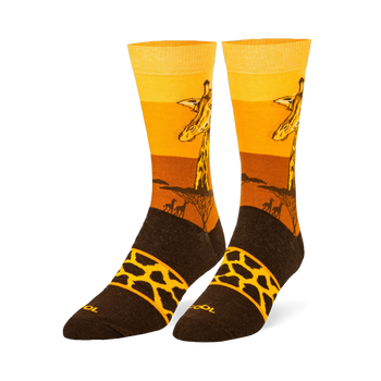 Crew socks showing a giraffe head against a yellow and orange sunset, tree silhouettes, and a brown foot with a spotted band.