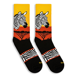 Flat lay of two Zebra Safari socks facing left, showing the sunset gradient, zebra head, tree silhouettes, and striped arch.