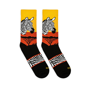 Flat lay of two Zebra Safari socks facing left, showing the sunset gradient, zebra head, tree silhouettes, and striped arch.