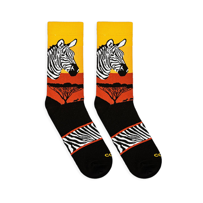 Flat lay of two Zebra Safari socks facing left, showing the sunset gradient, zebra head, tree silhouettes, and striped arch.