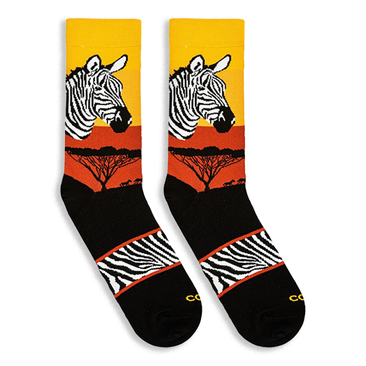 Flat lay of two Zebra Safari socks facing left, showing the sunset gradient, zebra head, tree silhouettes, and striped arch.