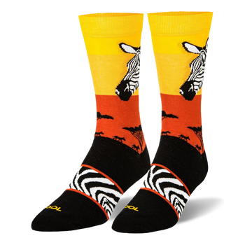 Black crew socks featuring a yellow and orange sunset, zebra head portrait, safari tree silhouettes, and an arch stripe band.