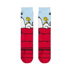 Flat lay of two crew socks side-by-side displaying Snoopy resting on a red doghouse with Woodstock under a blue sky.