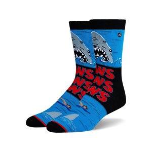 Pair of Jaws-themed crew socks. Blue, black, and red design features the Jaws movie poster with sharks and swimmers.