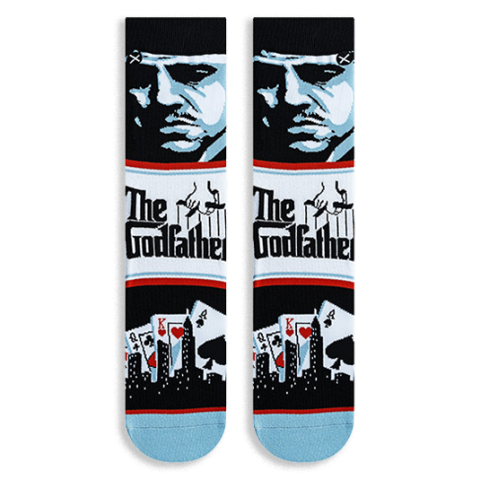 Flat lay of Godfather crew socks displaying a blue character portrait, The Godfather logo, and playing cards with a skyline.
